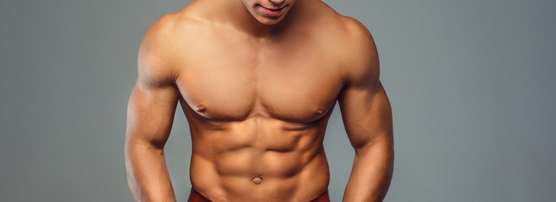 Muscular man with naked torso and hands in pockets. Isolated on grey background.